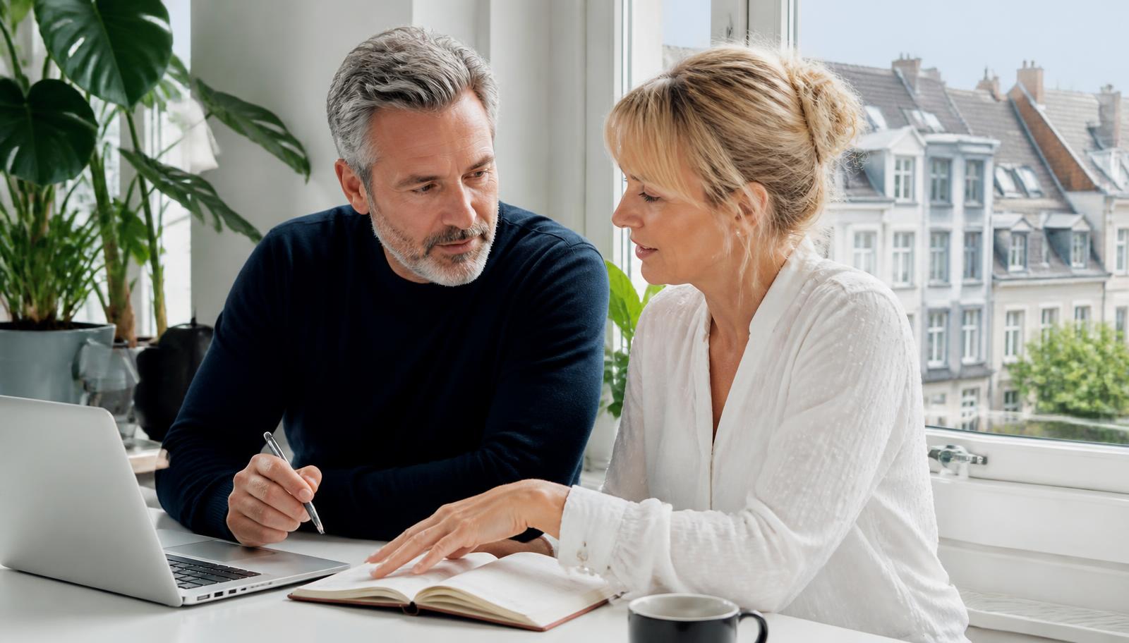 A couple planning together with a laptop and notebook by a window overlooking a European city